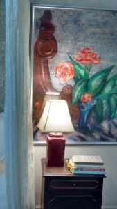 books on bedside table in front of painting of vase of flowers