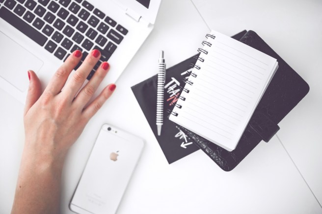 white laptop,black and white notepad and pen, white mobile, on desk