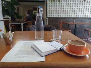 coffee cup, water, writing pad, pen on wooden table in cafe