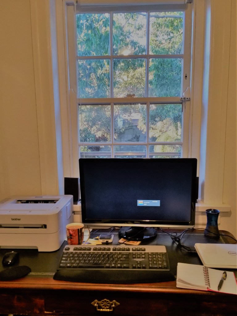 writing desk with keyboard, screen and printer in front of window