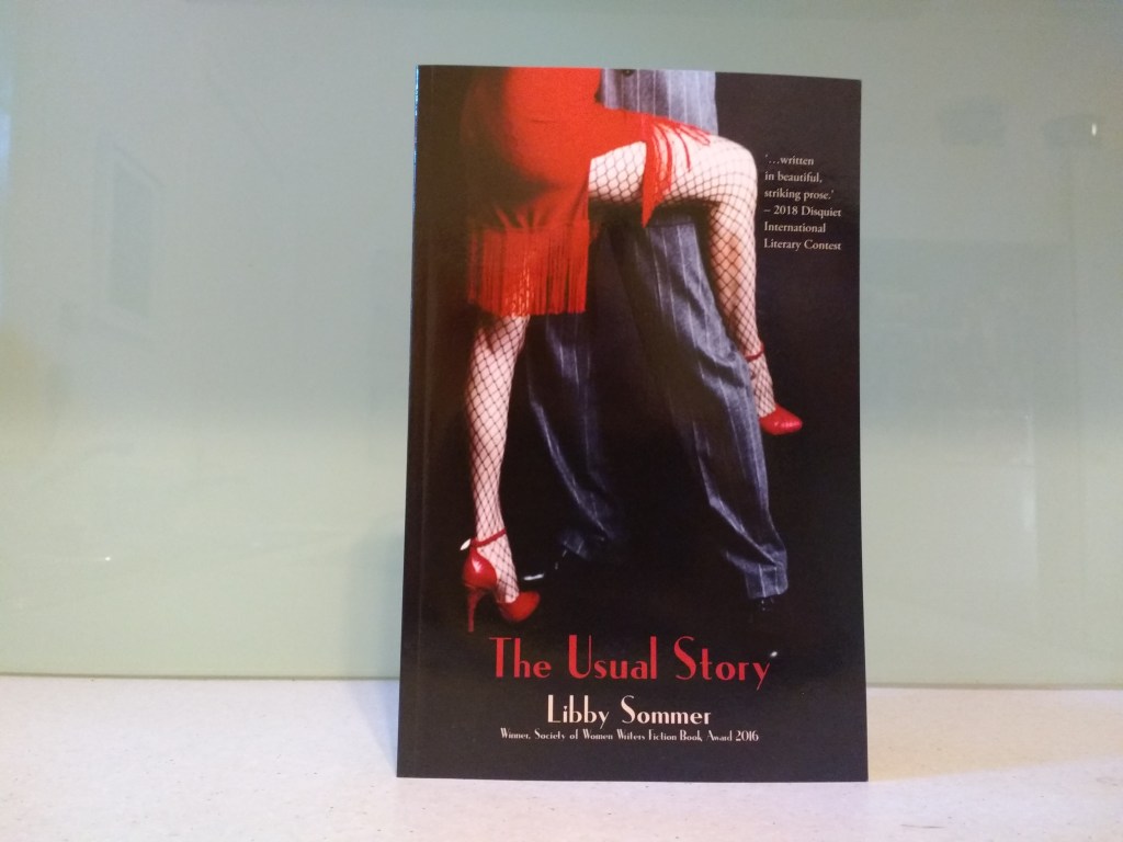 a grey-suited man and a woman in a red fringed dress, red shoes and fishnet stockings, are in a tango stance, her leg wrapped around him.