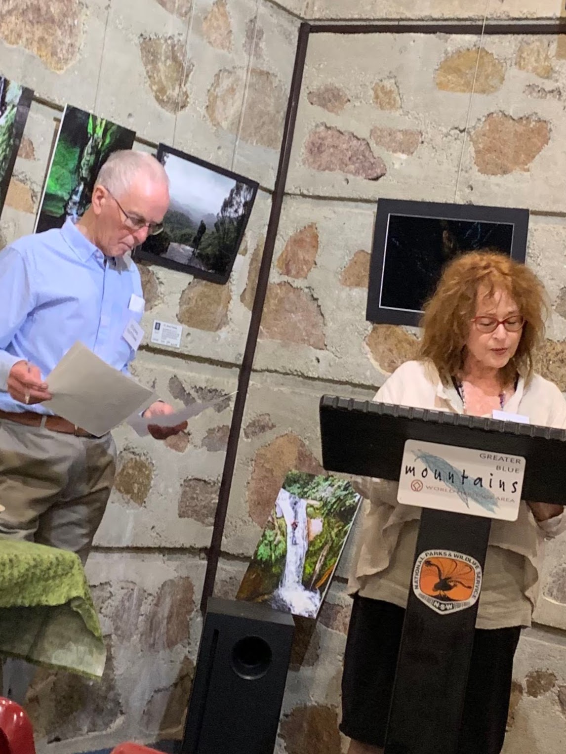 Libby Sommer reading her poem at podium watched by publisher Stephen Matthews